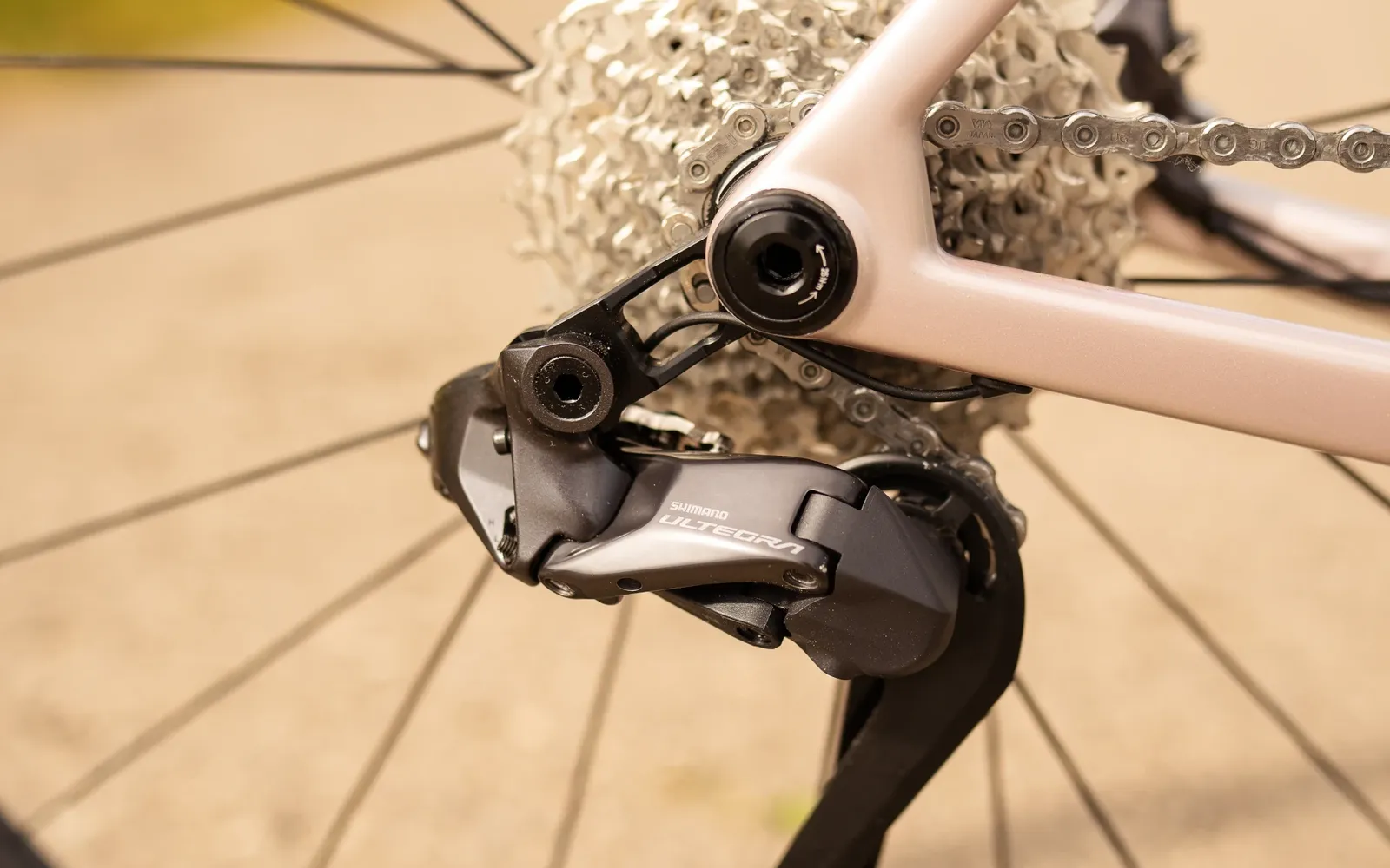 Nahaufnahme eines Shimano Ultegra Schaltwerks an einem beigen Fahrradrahmen mit silberner Kassette und Kette am Hinterrad.