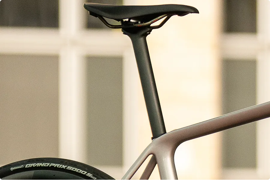 Schwarz glänzender Fahrradsattel und Sattelstütze auf mattgrauem Rahmen. Ein Continental Grand Prix 5000 Reifen ist teilweise sichtbar.