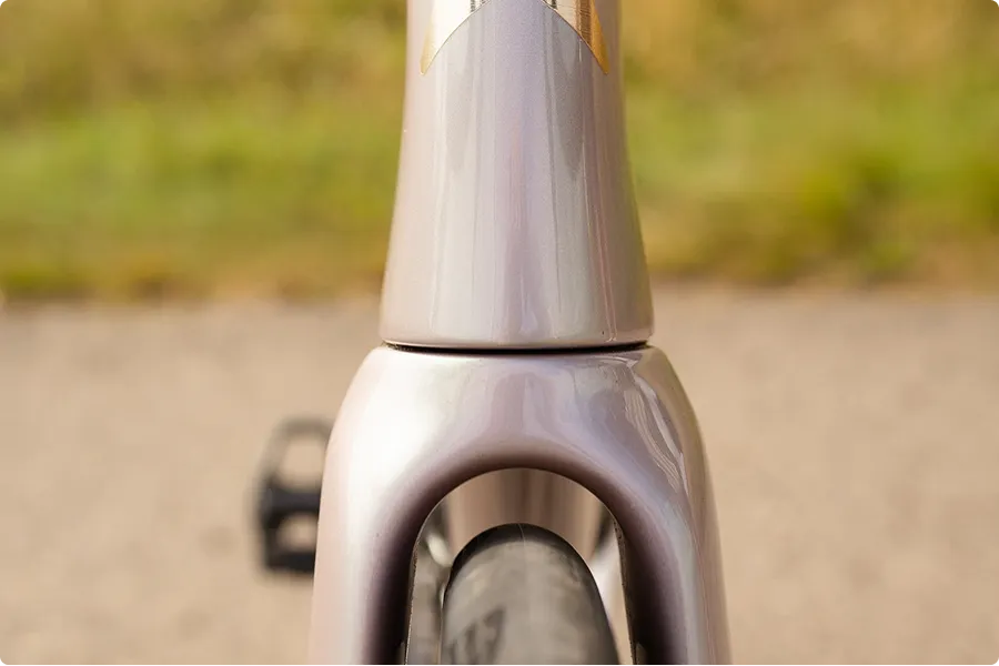 Vorderansicht des glänzenden, lichtlila-silbernen Fahrrad-Lenkkopfs und der Gabel mit sichtbarem Reifen.