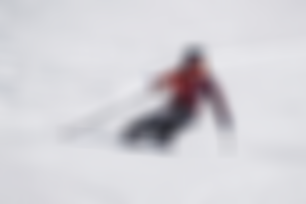 Skier carving down a groomed ski slope on a snowy winter day.