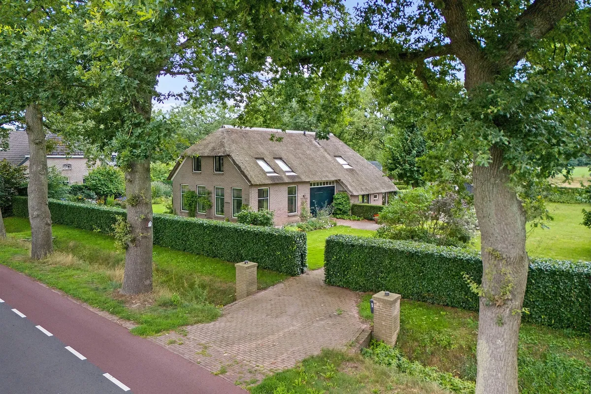 Vrijstaande woning met rieten kap achter een haag en hoge eiken