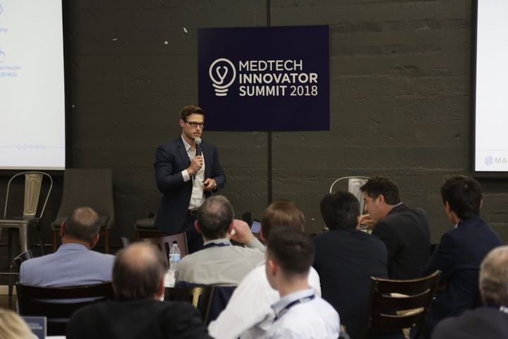 Speaker presenting in front of the MedTech Innovator Summit 2018 sign