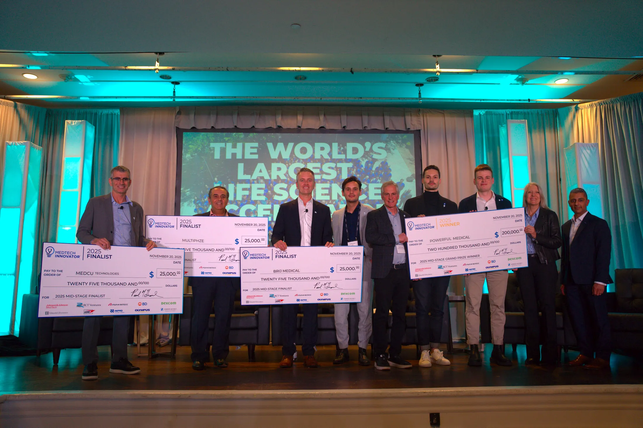 Finalists and judges holding prize cheques on stage at the 2025 MedTech Innovator Mid-Stage Finals