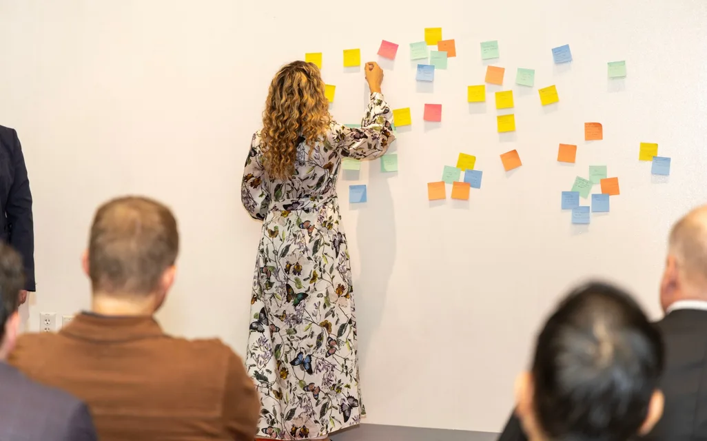 A workshop participant arranging colorful sticky notes on a wall as founders look on