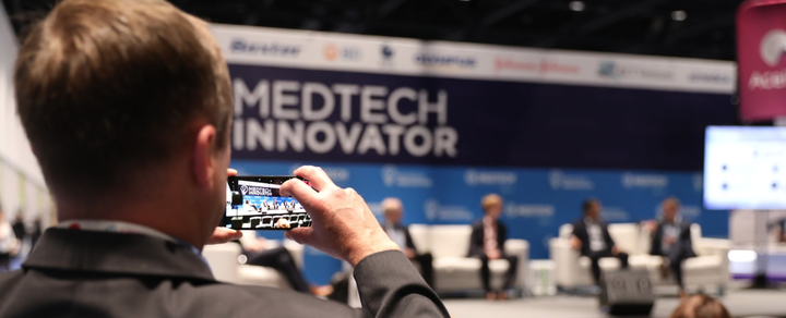 Attendee photographing a panel on his phone in front of the MedTech Innovator stage