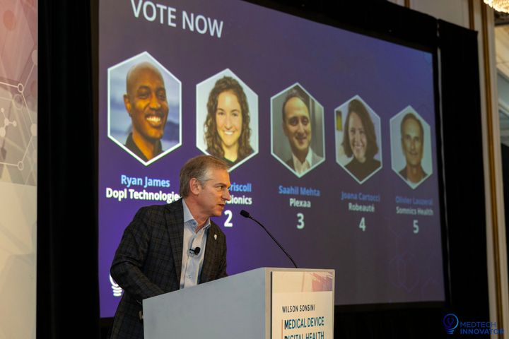 Presenter at the lectern in front of the "Vote Now" screen showing the five 2024 Vision Award finalists