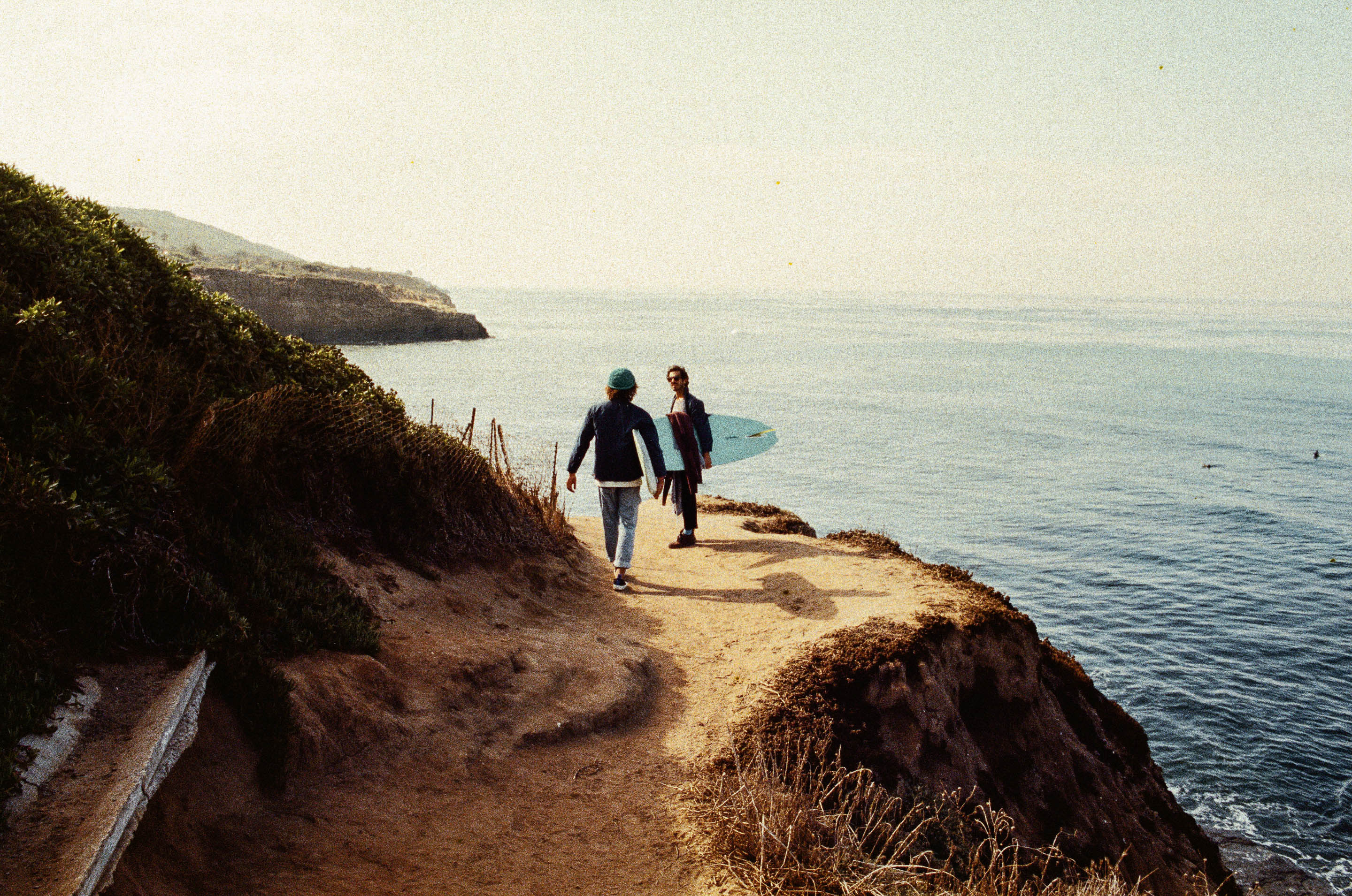 Two surfers walking the cliff path above the water at Oceanside.