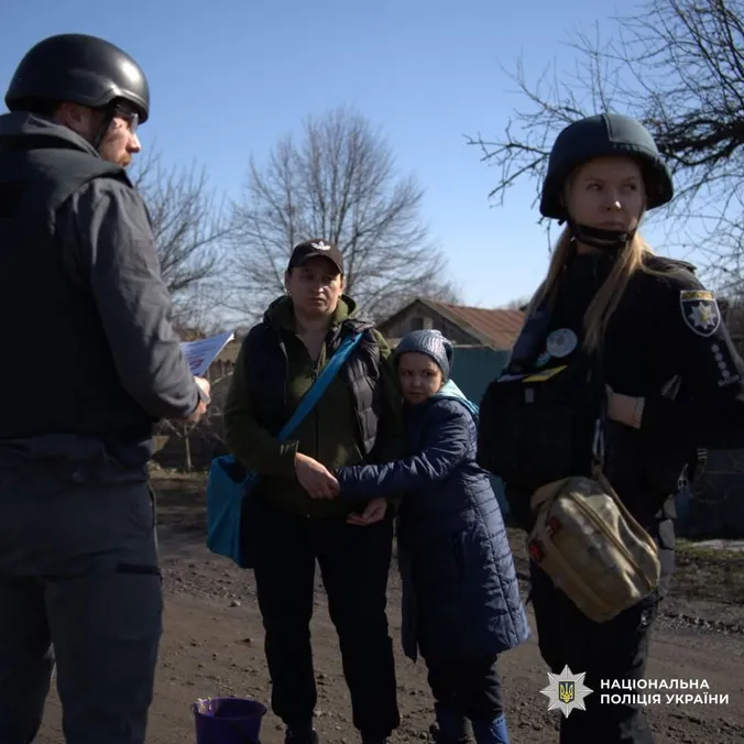 Politifolk i hjelm og skudsikker vest taler med en mor og hendes barn på en grusvej i Ukraine.