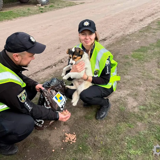 To ukrainske politifolk sidder på hug på en grusvej med en hvalp og en pose hundefoder.
