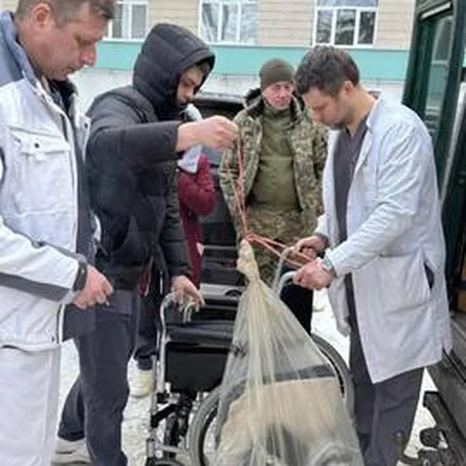 Mænd i hvide kitler og vinterjakker samles om forsyninger og en kørestol i sneen