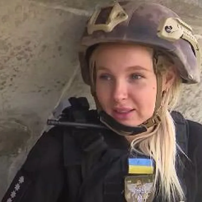 Kvinde i hjelm og skudsikker vest med et ukrainsk flag på uniformen kigger mod kameraet.