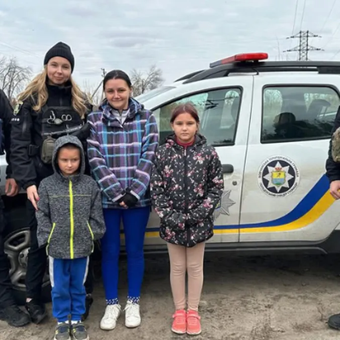 Ukrainske politifolk står sammen med en kvinde og to børn foran en politibil på en landevej.