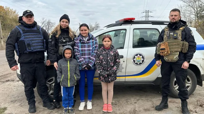 Ukrainske politifolk står sammen med en kvinde og to børn foran en politibil på en landevej.