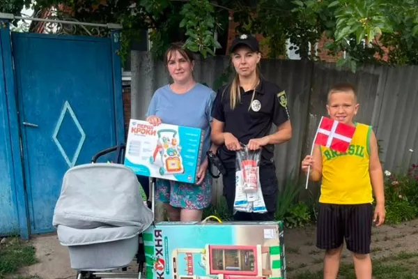 Kvinde, ukrainsk politibetjent og dreng med lille dansk flag står ved en barnevogn og udleveret legetøj.