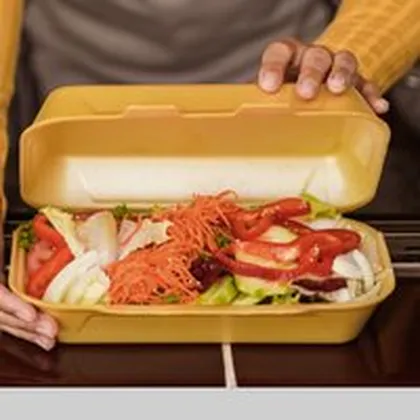 Hände halten gelbe Menübox mit Salat