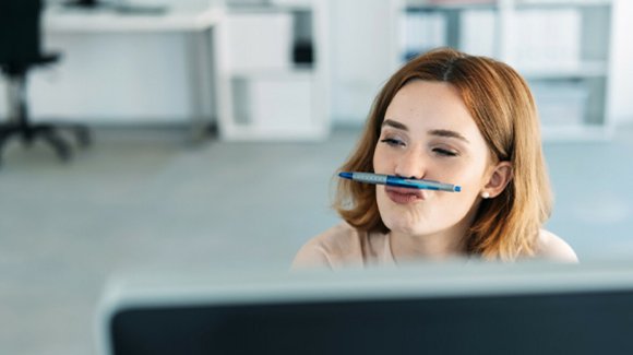 Frau im Büro balanciert einen Stift auf der Oberlippe
