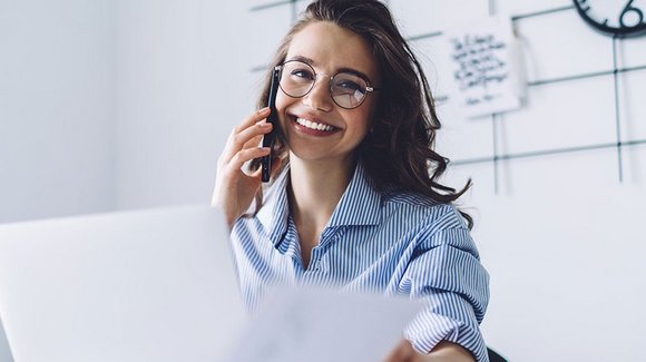 Frau mit Brille telefoniert im Büro mit Unterlagen