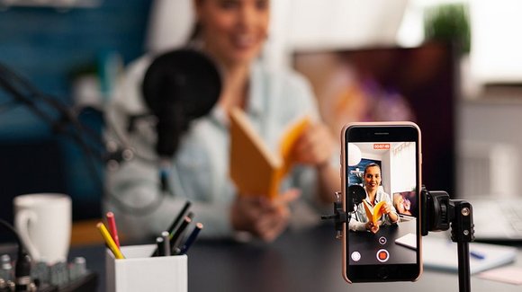 Smartphone auf Stativ filmt eine Frau mit Buch