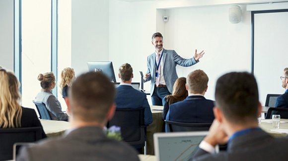 Referent mit ausgebreiteten Armen vor sitzendem Publikum