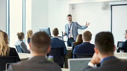 Referent mit ausgebreiteten Armen vor sitzendem Publikum