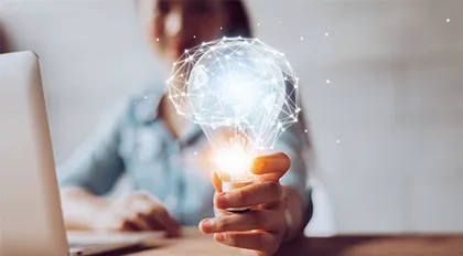 Hand hält leuchtende Glühbirne aus Lichtlinien vor Laptop