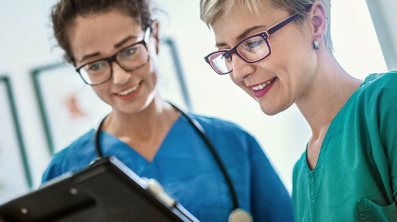 Zwei Pflegekräfte in Kasacks blicken auf ein Klemmbrett