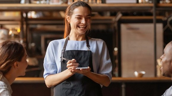 Lachende Servicekraft mit Schürze und Notizblock im Lokal