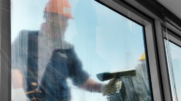 Reinigungskraft putzt ein Fenster mit Abzieher