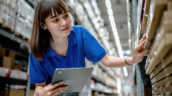 Mitarbeiterin im blauen Polo mit Tablet am Lagerregal