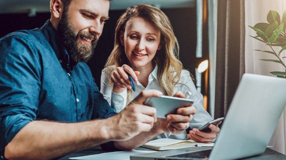 Mann und Frau am Laptop, Smartphone in der Hand