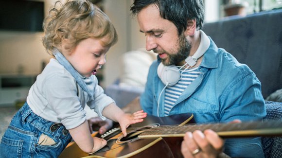 Mann und Kleinkind an einer Akustikgitarre