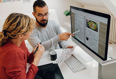 Frau und Mann besprechen einen Produktkatalog am Bildschirm