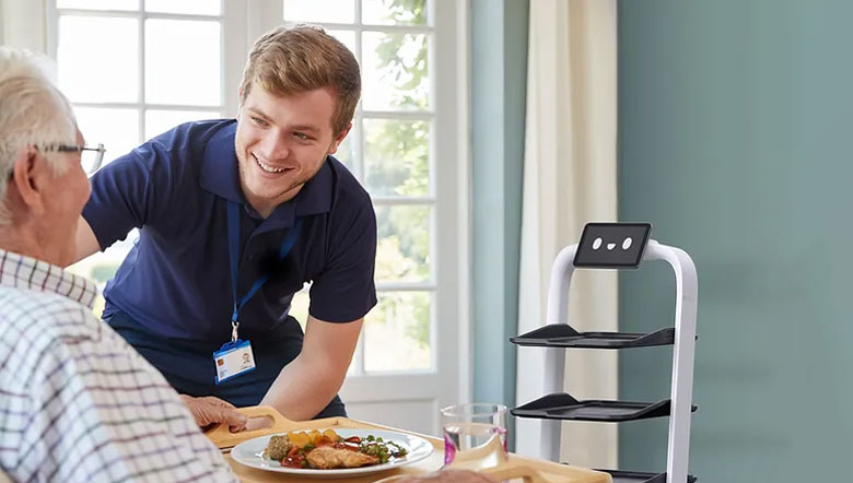 Pflegekraft serviert Essen, daneben ein Serviceroboter mit Tabletts
