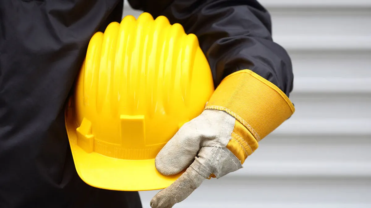 Person hält gelben Schutzhelm unter dem Arm