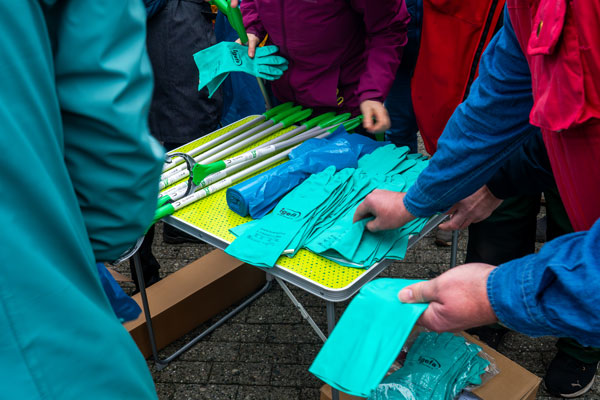 Hände verteilen türkise Handschuhe und Müllzangen am Tisch