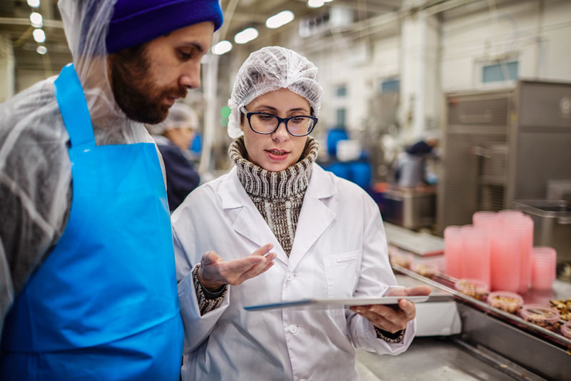 Zwei Beschäftigte in Schutzkleidung mit Tablet in der Lebensmittelproduktion