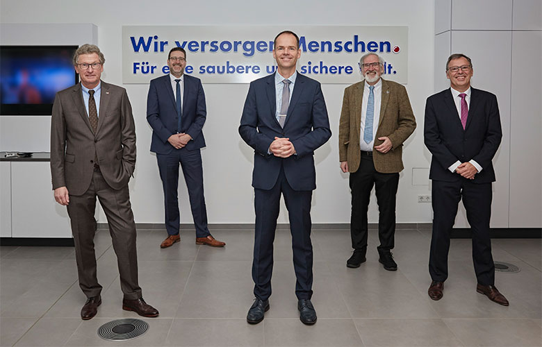 Fünf Männer im Anzug vor dem Schriftzug Wir versorgen Menschen