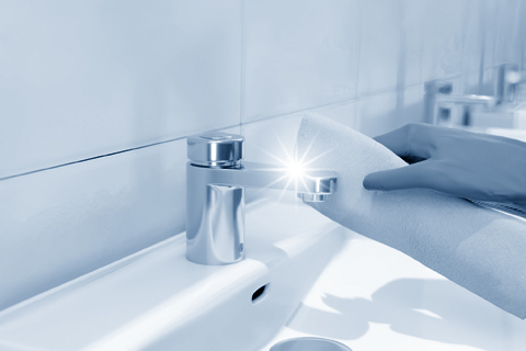 Behandschuhte Hand reinigt Armatur am Waschbecken