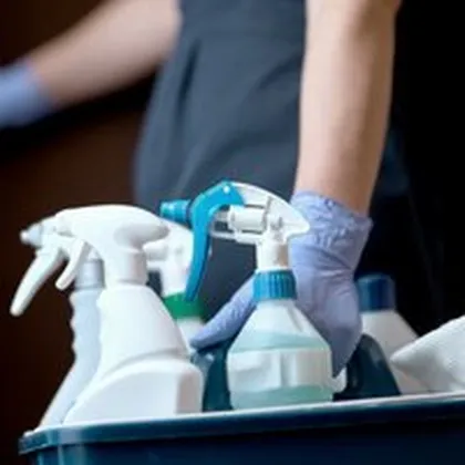 Hand mit Handschuh greift Sprühflaschen im Putzeimer