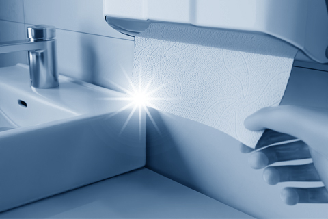 Hand zieht Papierhandtuch aus Spender über Waschbecken