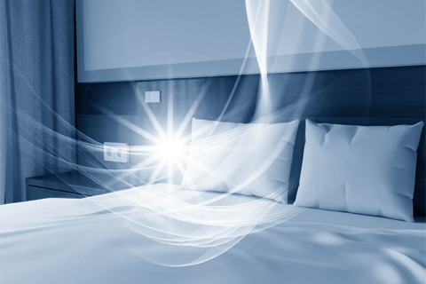Hotelbett mit Lichtschleiern über dem Kopfkissen