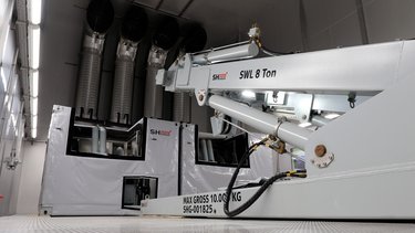 Interior of an industrial facility with large machinery, including an articulated arm labeled "SWL 8 Ton," and ventilation systems in the background.