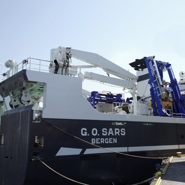 Research vessel G.O. Sars docked, featuring cranes and equipment on deck under clear skies.