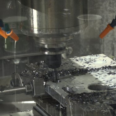 A CNC machine with rotating drill, cutting metal while coolant is applied, surrounded by metal shavings.