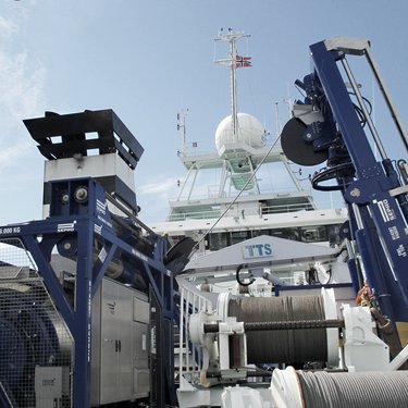 Deck of a ship equipped with large industrial machinery, including cranes and winches, under a clear blue sky.