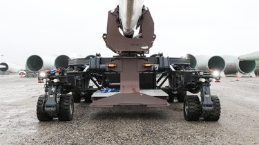 Heavy machinery with large wheels positioned on a gravel surface, holding a cylindrical object, surrounded by other similar structures.