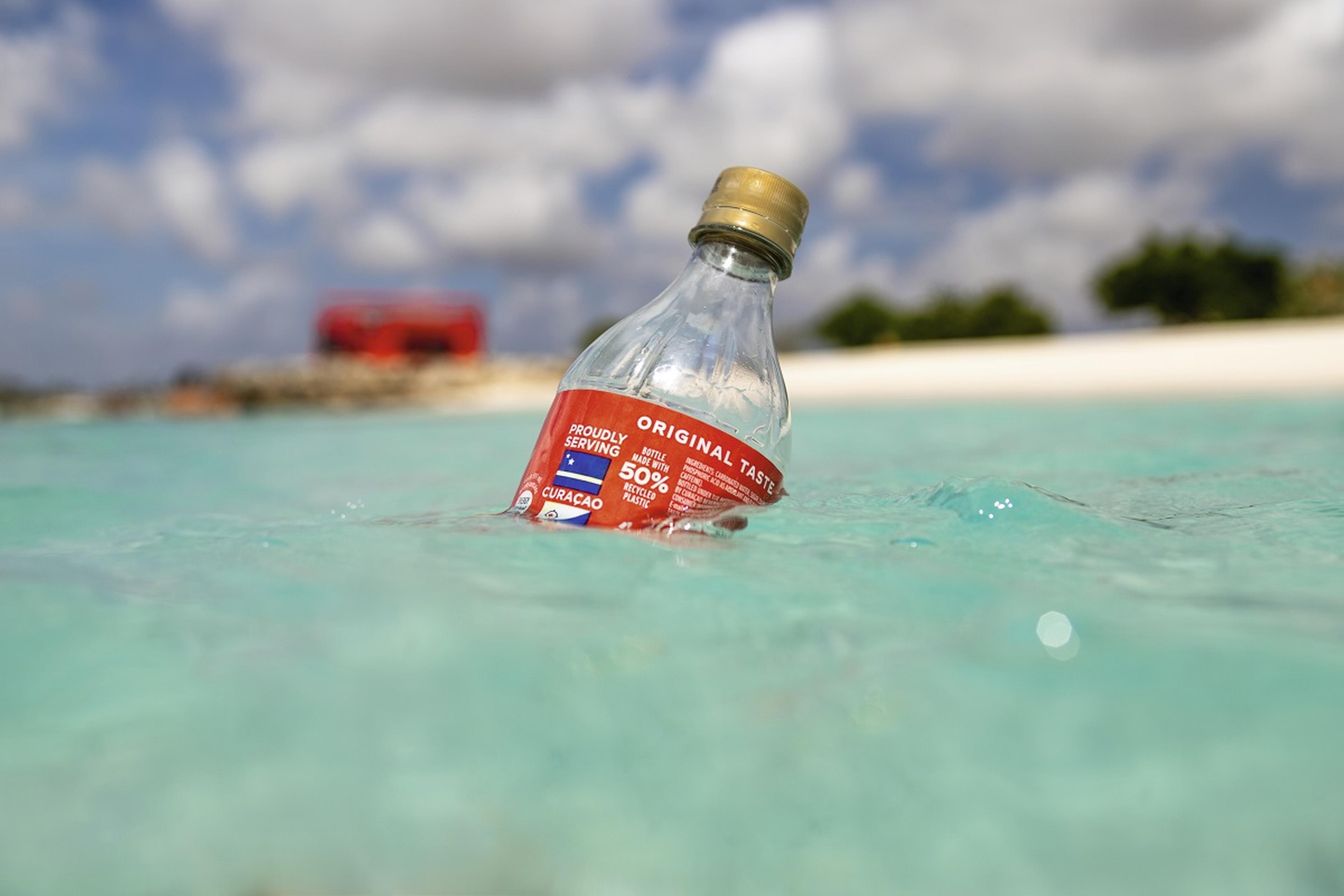 Plastic cola flesje drijft in het water langs strand