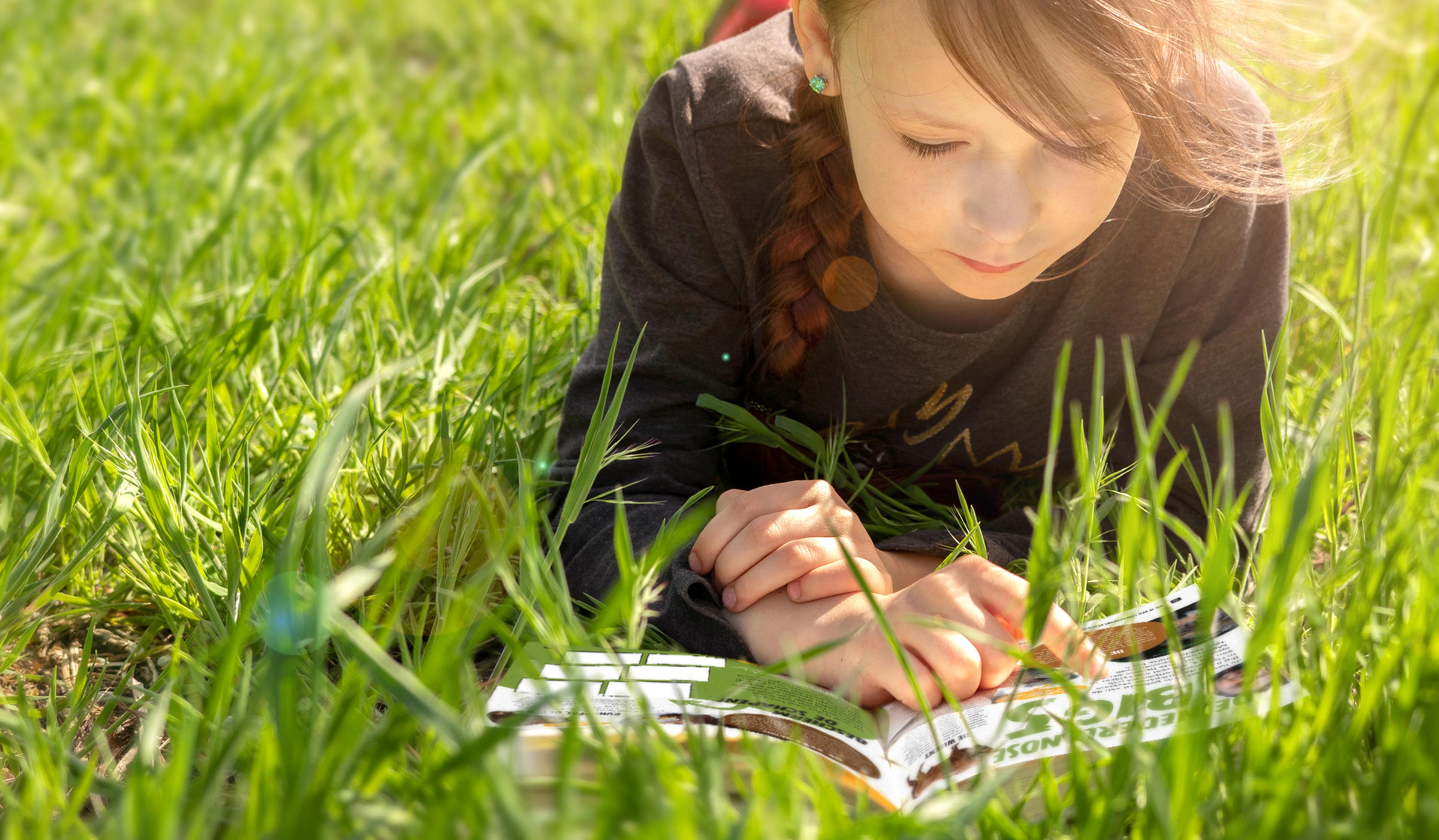 Meisje ligt in het gras een magazine te lezen