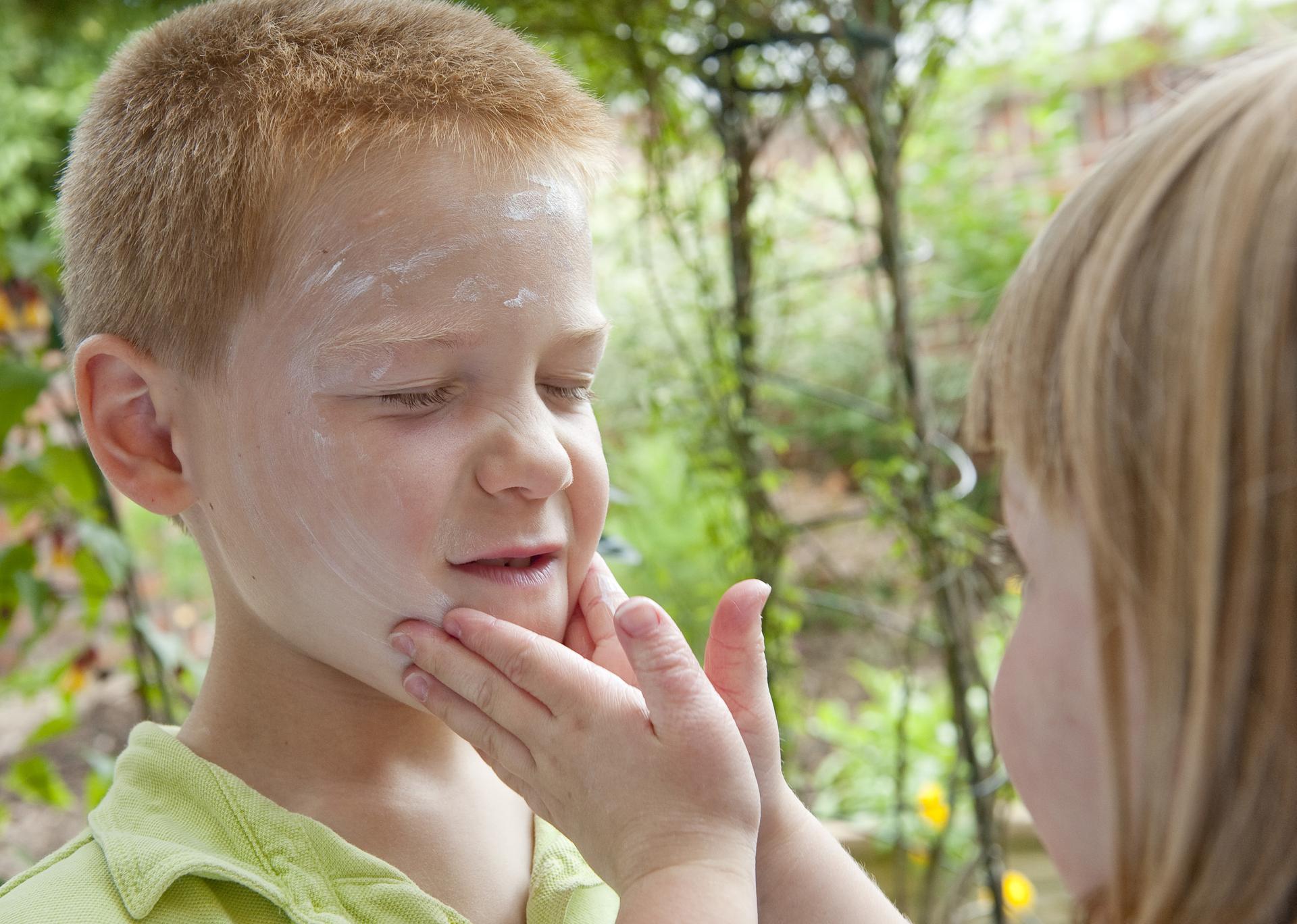 meisje smeert gezicht van jongen in met zonnebrandcreme
