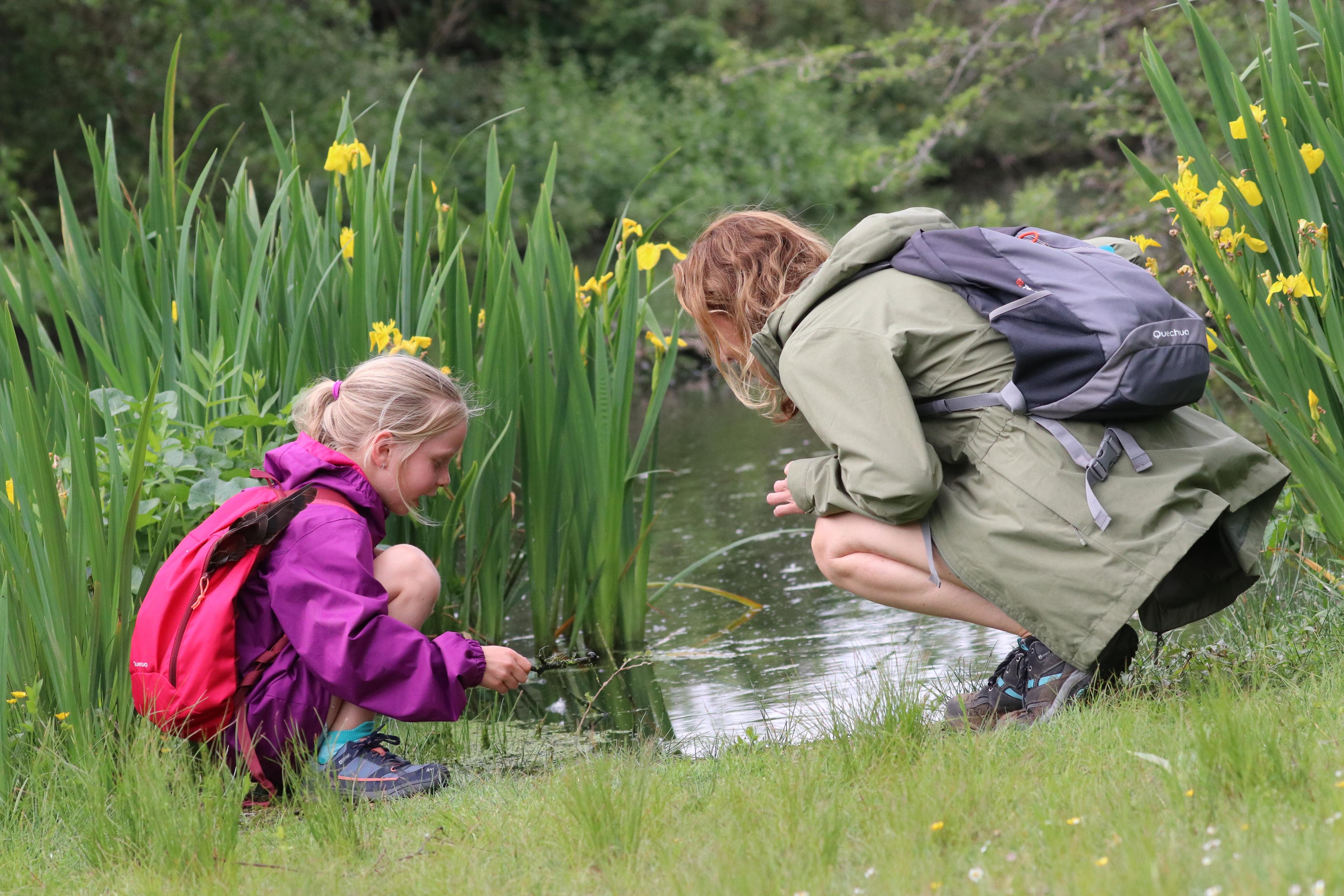 Vrouw en kind in de Nederlandse natuur bij een kleine rivier, op zoek naar kleine dieren.